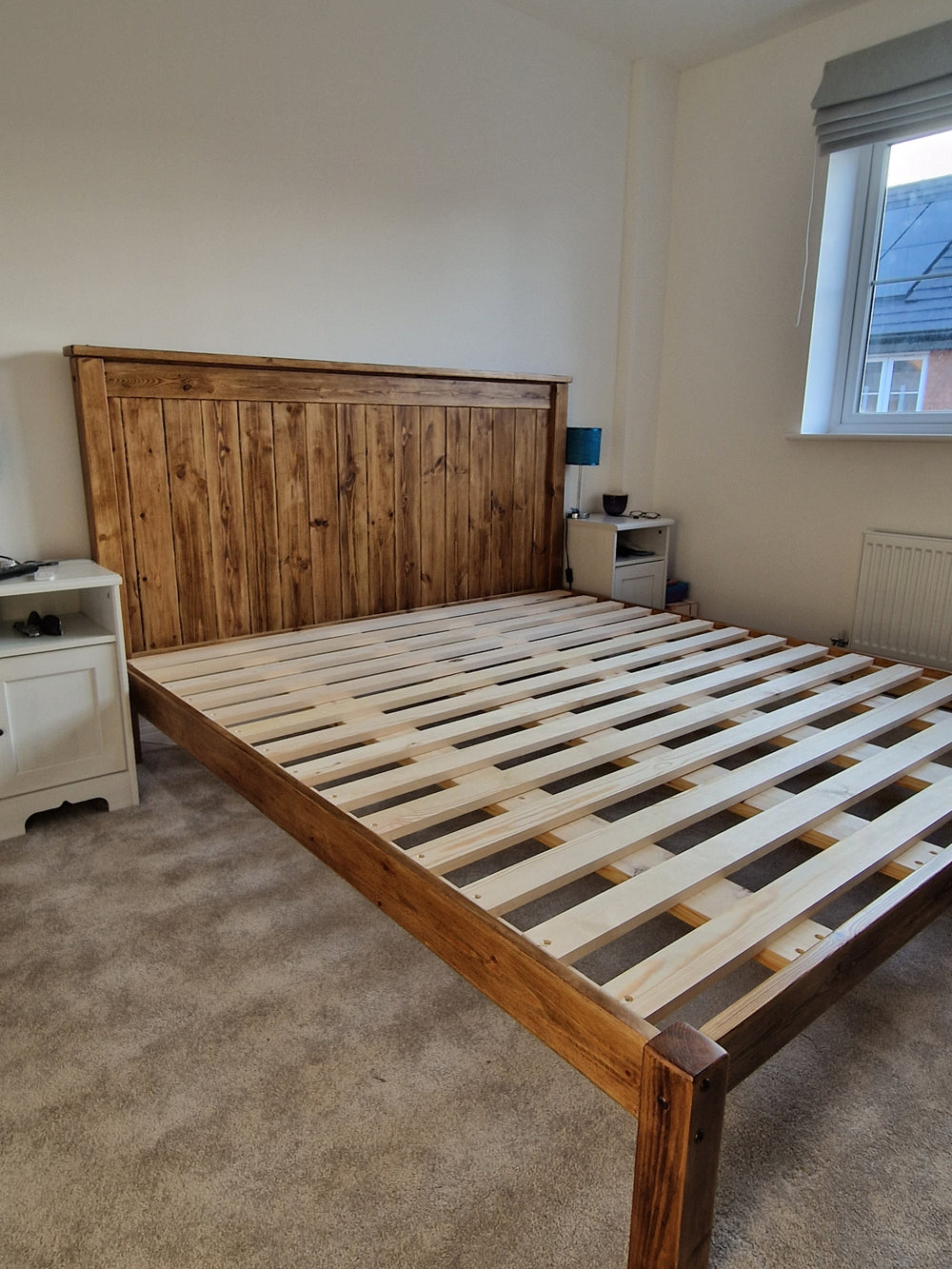 Wooden bed frame in a room with carpeted floor and a window.