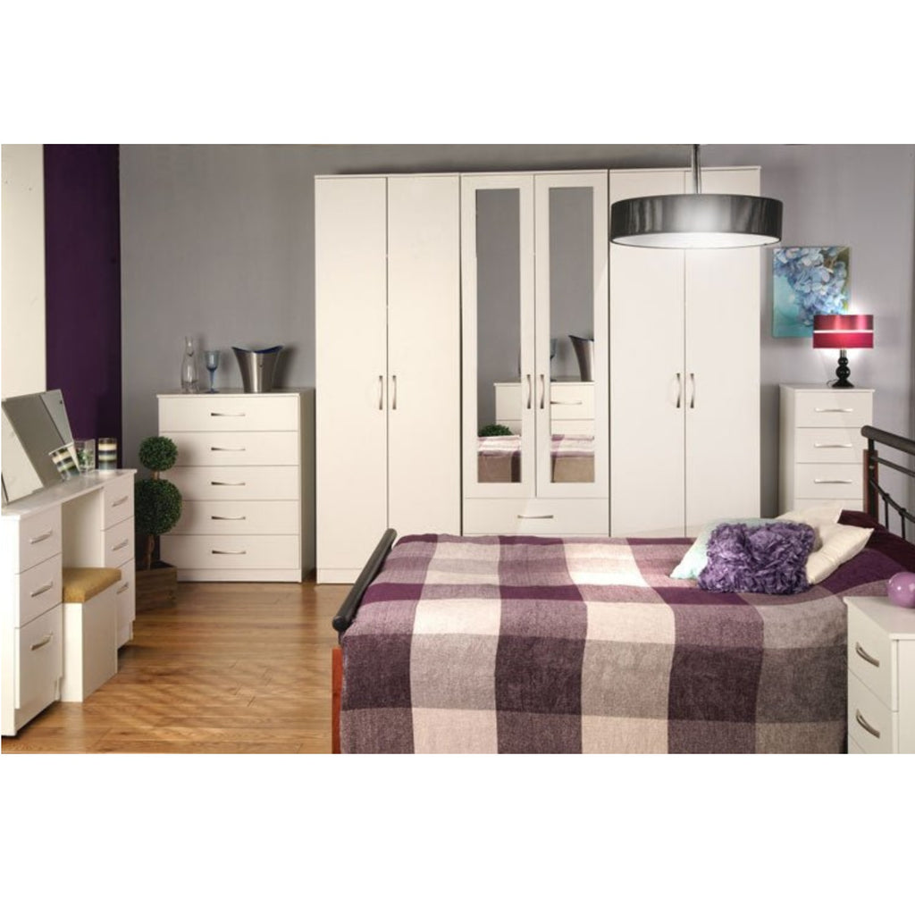 JJ Bedroom range - 7 pieces of furniture from the JJ bedroom range set out in a large bedroom, with a bed at the forefront and various decorations throughout - Beds4us