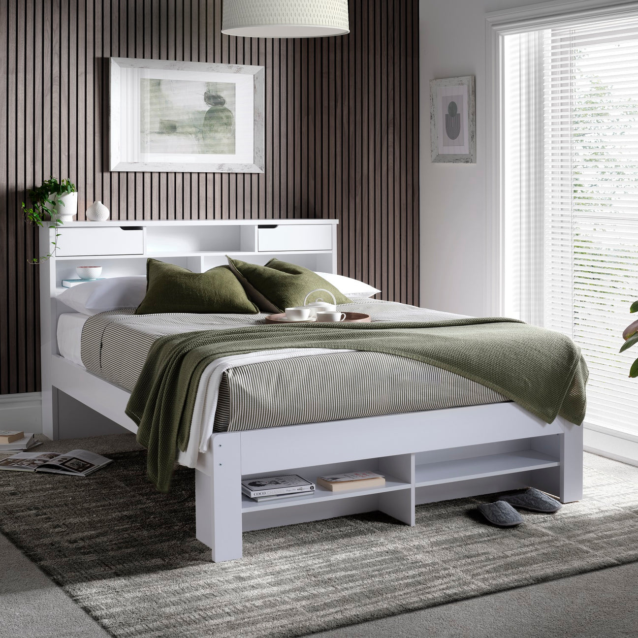 A modern white bed frame with integrated headboard and storage shelves, styled with green and grey bedding in a contemporary bedroom setting.