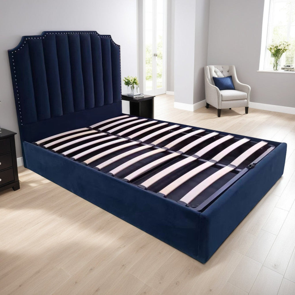 Selkirk Ottoman Storage Bed - Navy blue plush velvet fabric ottoman bed frame positioned at an angle, showing the slats, in a modern bedroom - Beds4Us